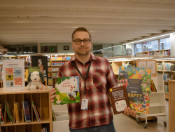 Lastenosastolla kirjahyllyjen edessä seisova Antti pitää käsissään ukrainankielisiä lastenkirjoja ja hymyilee. Kuva Tytti Tyrväinen